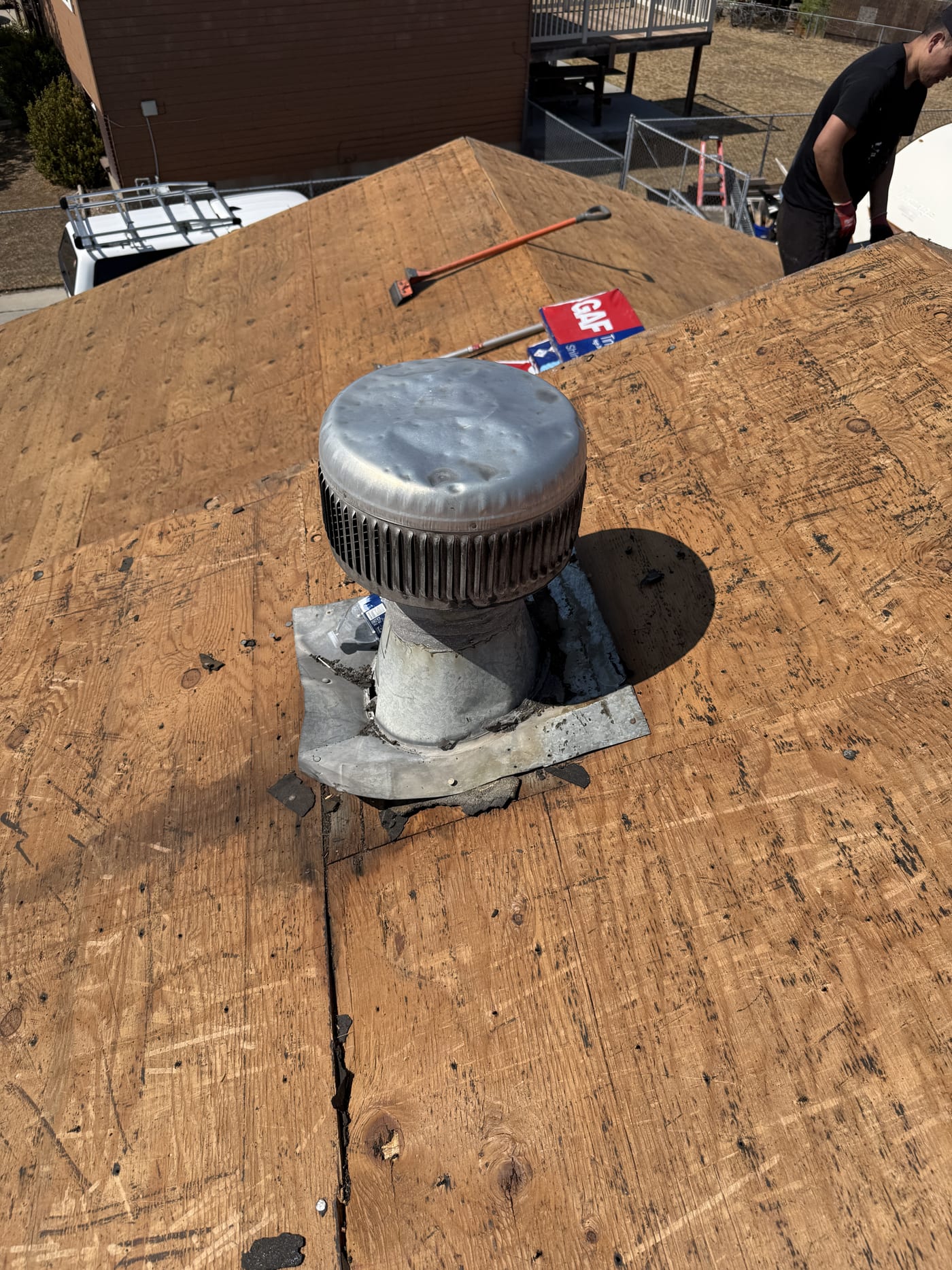 Close-up of roof vent pipe boot on bare OSB roof deck during re-roof, GAF materials visible in background