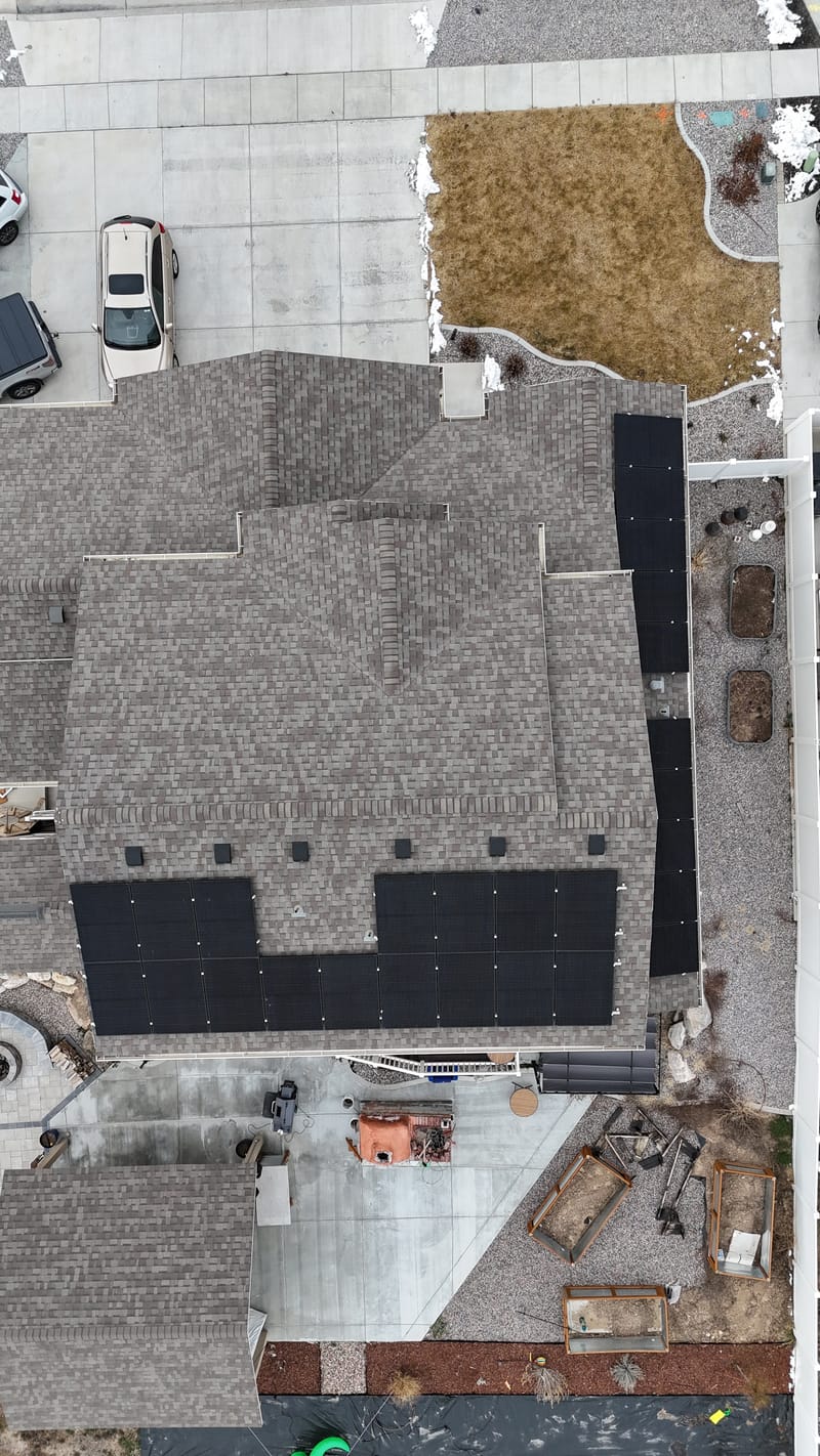 [Trina panels] Drone top-down aerial of completed solar array across two roof sections of residential home, construction equipment visible nearby