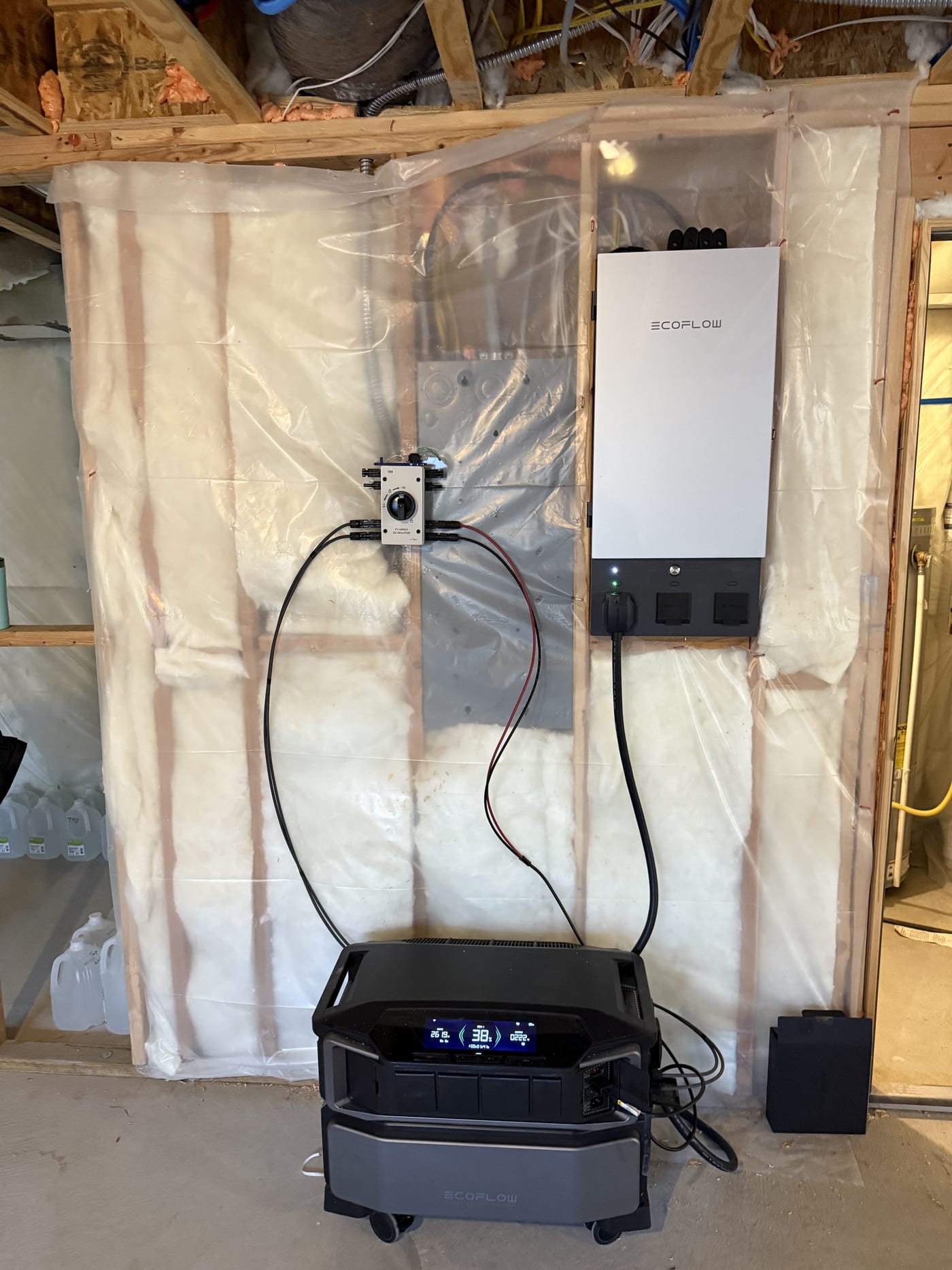 EcoFlow DPU inverter (white) and EcoFlow SHP2 battery unit staged on a wood pallet with plastic sheeting in a garage, prior to permanent installation