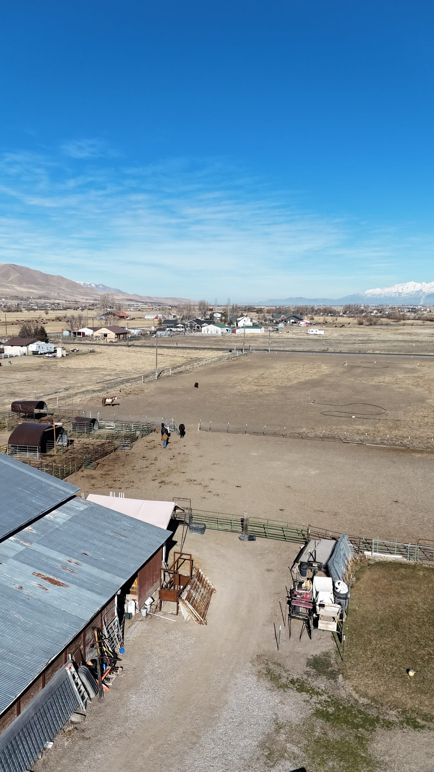 Sideways drone aerial of rural ranch property with barns and open land — no solar panels or snow visible; appears to be a pre-installation site photo