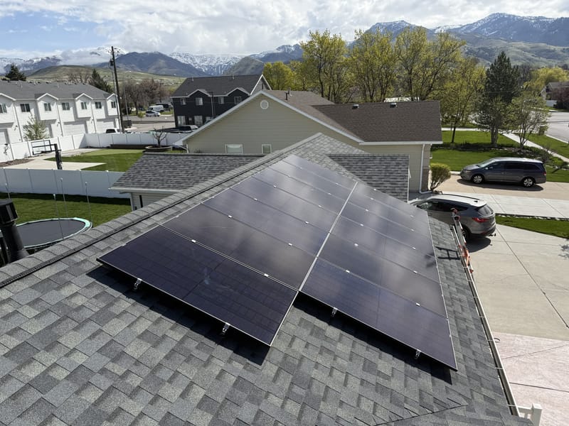 [black-on-black panels] Roof-level view of solar panels with driveway and street below