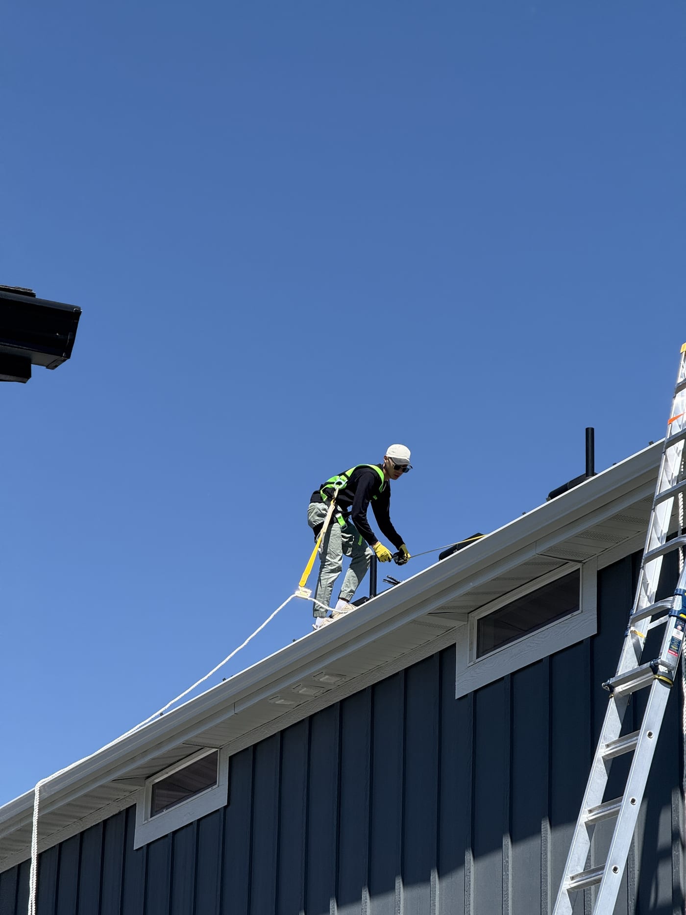 Worker with hard hat climbing to roof, clear blue sky background