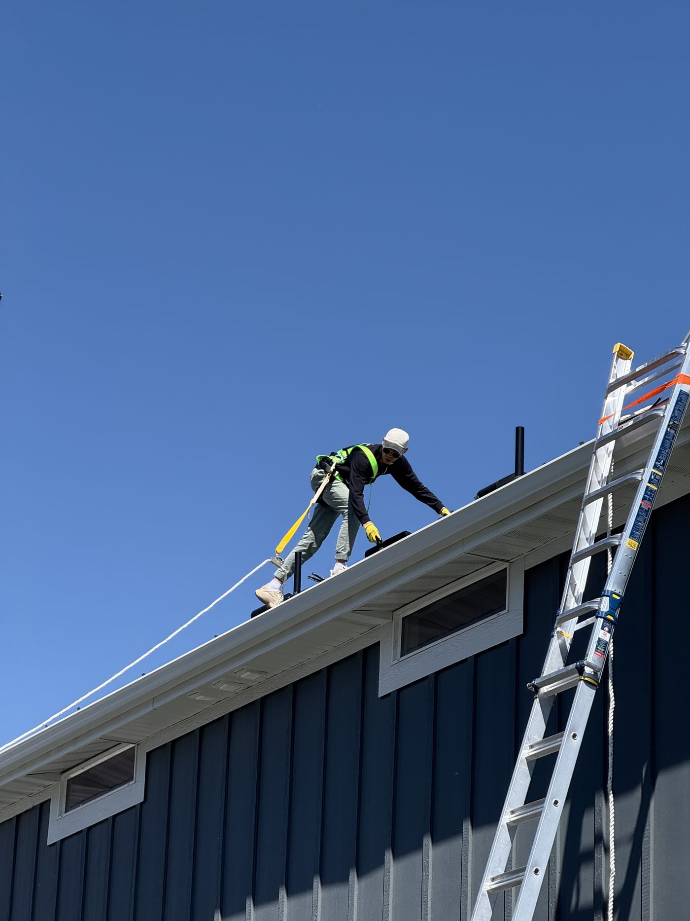Worker ascending ladder on blue house with safety equipment