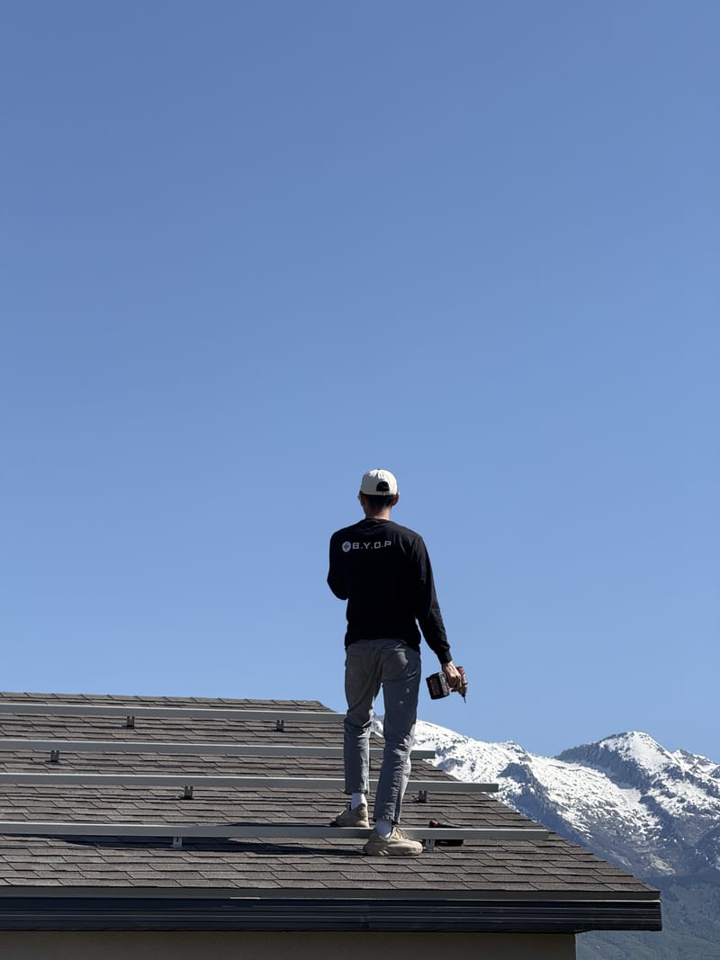 BYOP crew member on roof with snow-capped mountains in background during solar installation