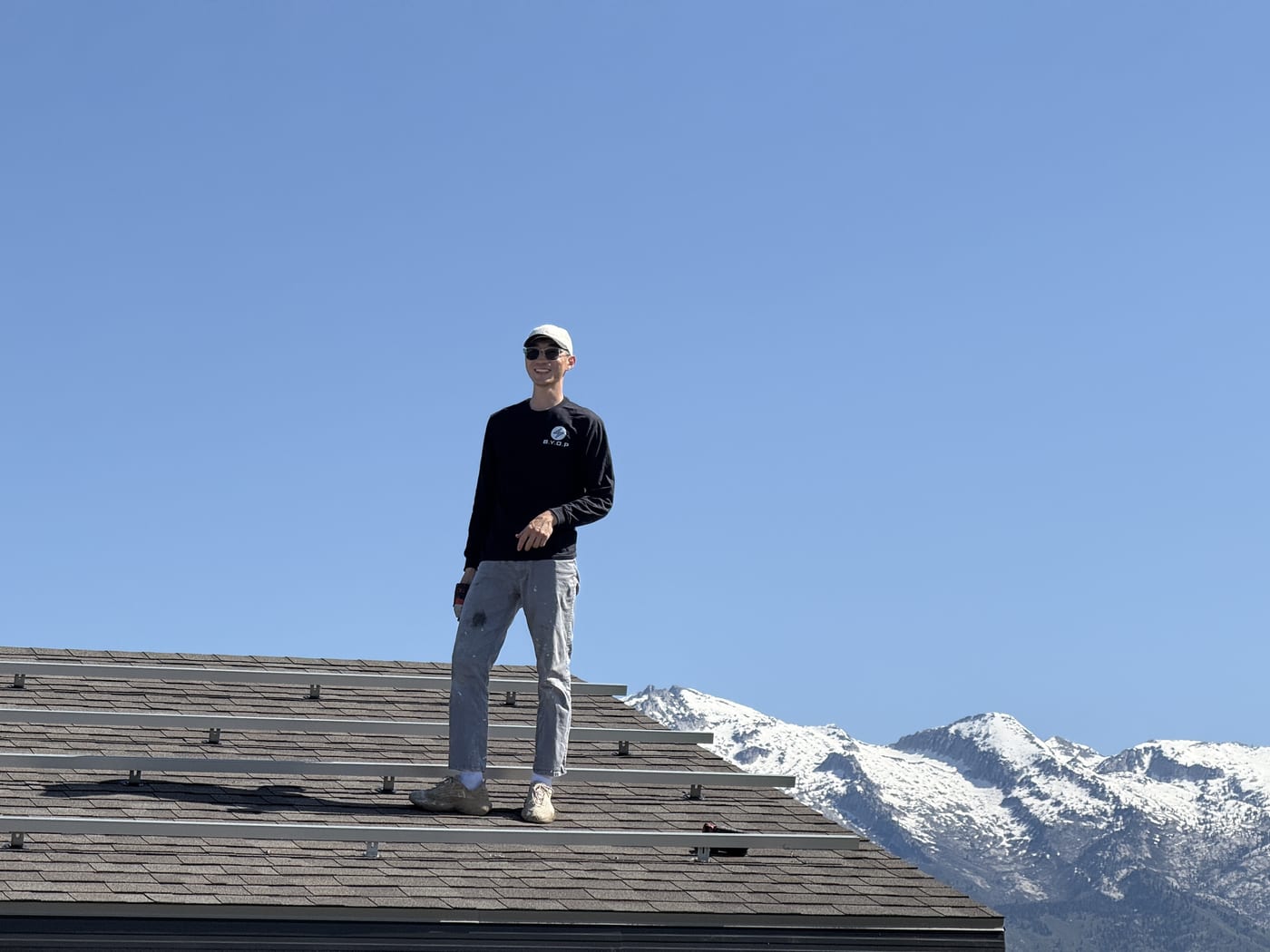 BYOP installer standing on roof beside solar panels with snow-capped mountains behind