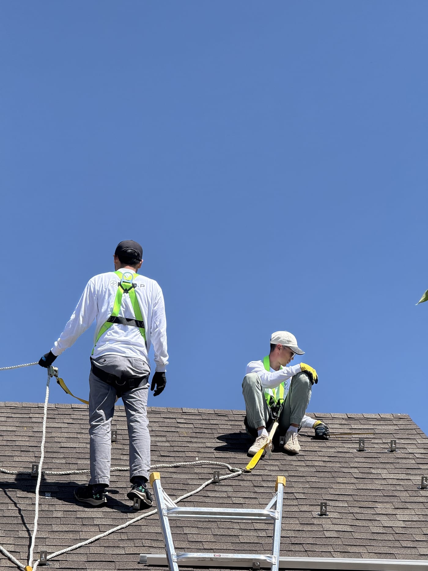 Two crew members in safety harnesses standing on roof during racking installation against blue sky
