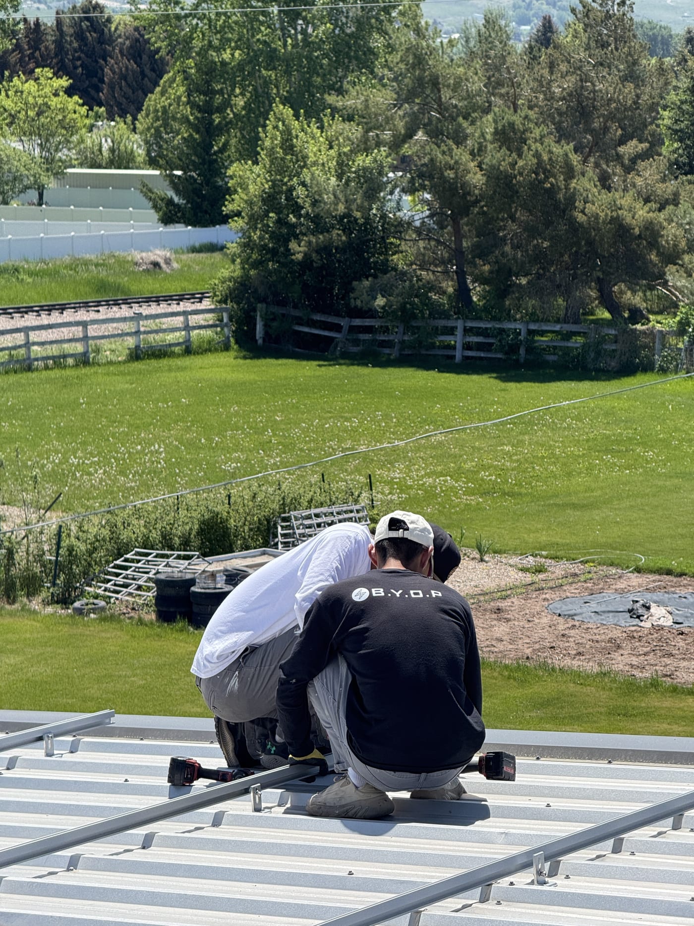 Two BYOP crew members working on metal roof edge during racking installation with green yard below
