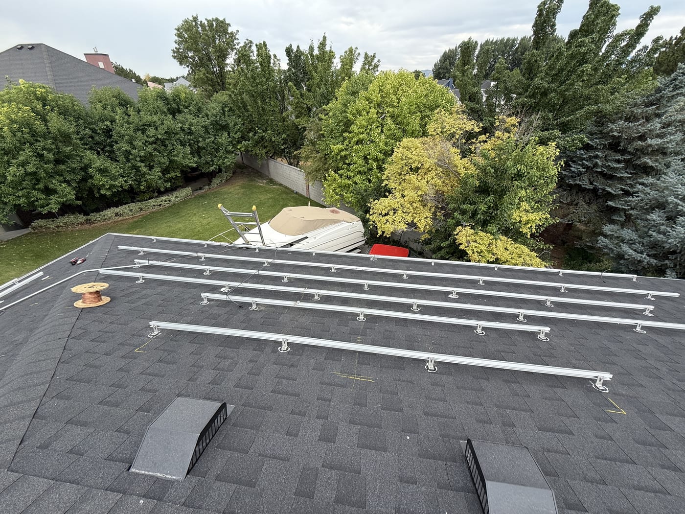 Wide view of racking rails on dark shingle roof looking down to yard and trees