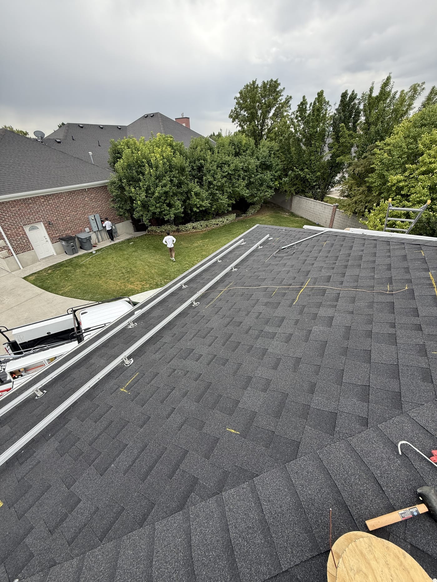 Racking rails on dark shingle roof looking down toward neighborhood on overcast day