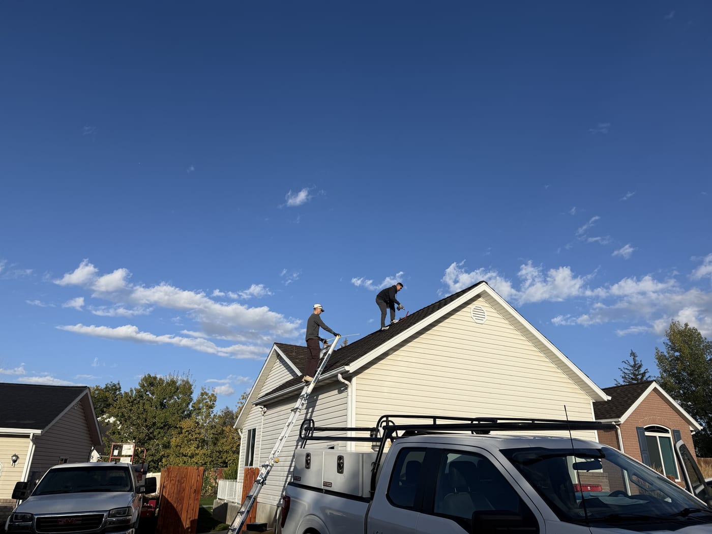 Worker climbing ladder to vinyl siding house roof with blue sky and clouds