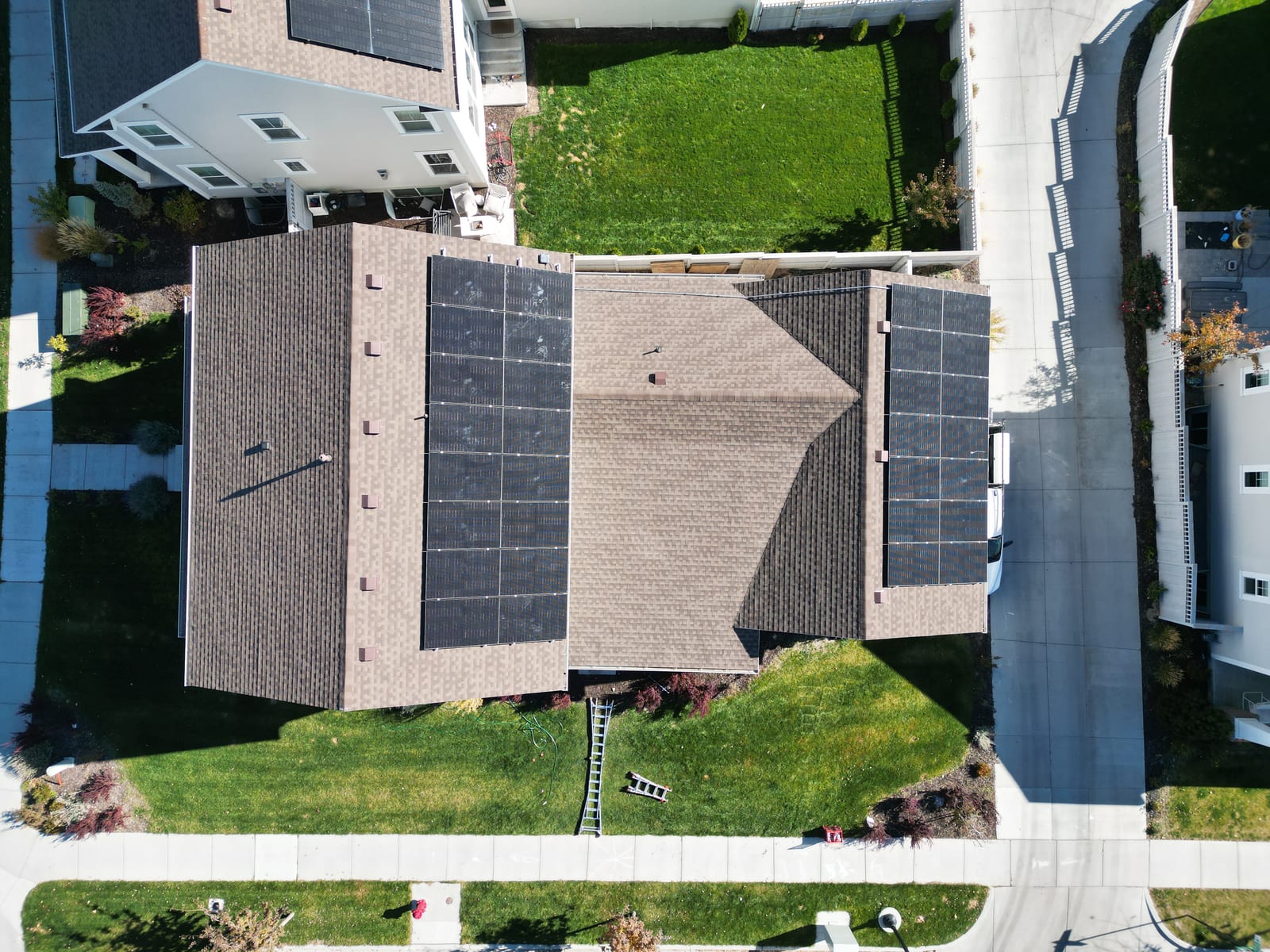 Drone top-down aerial showing solar panels on multiple roof planes with green yards and neighborhood