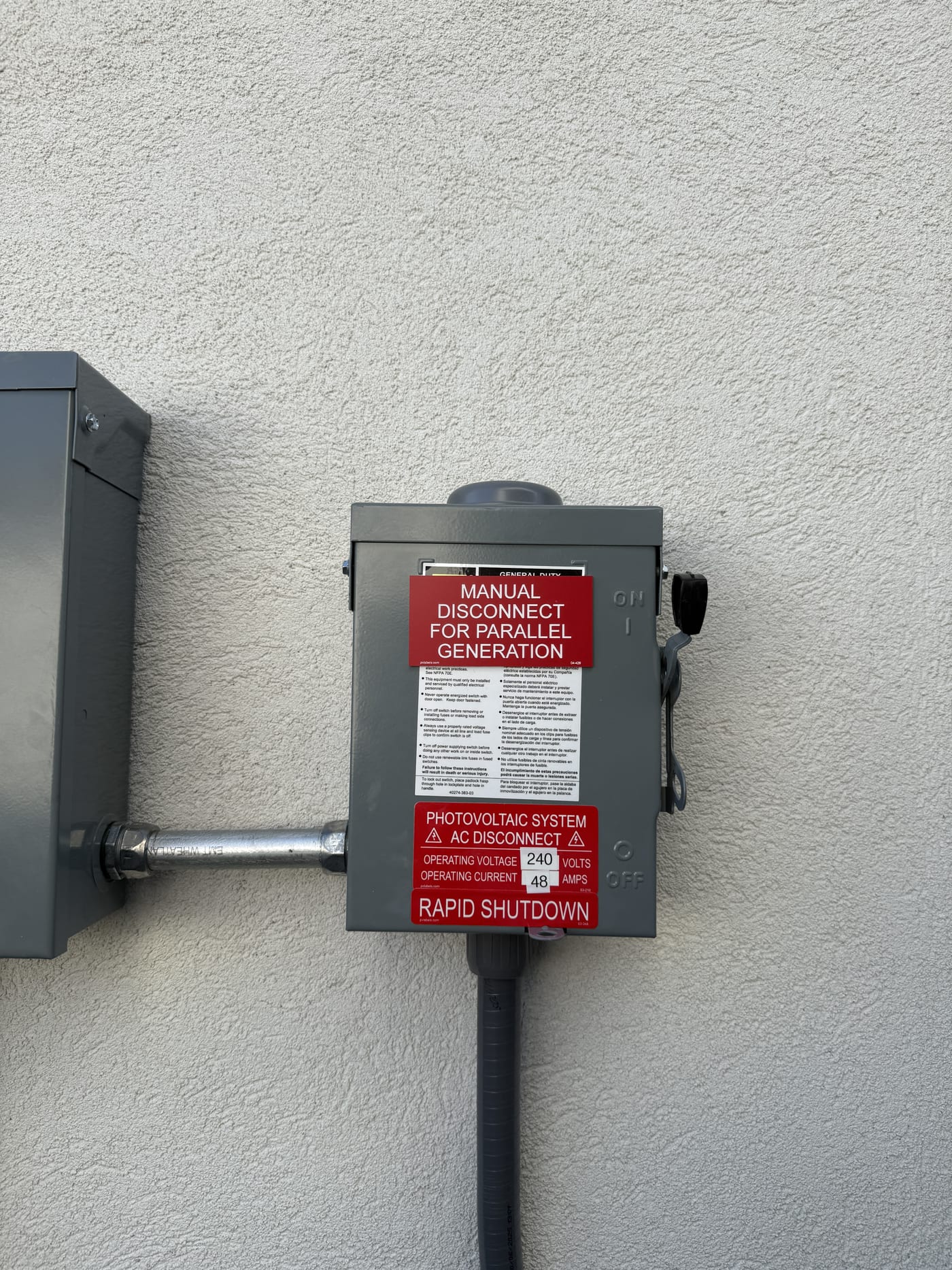 AC disconnect with Manual Disconnect for Parallel Generation and Rapid Shutdown labels on stucco wall