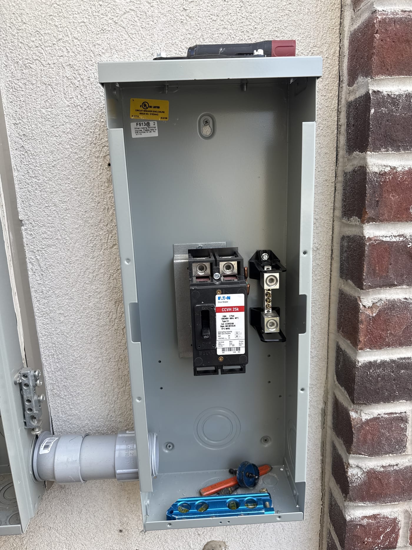 Open disconnect box with Eaton breaker and conduit mounted on exterior stucco wall near brick