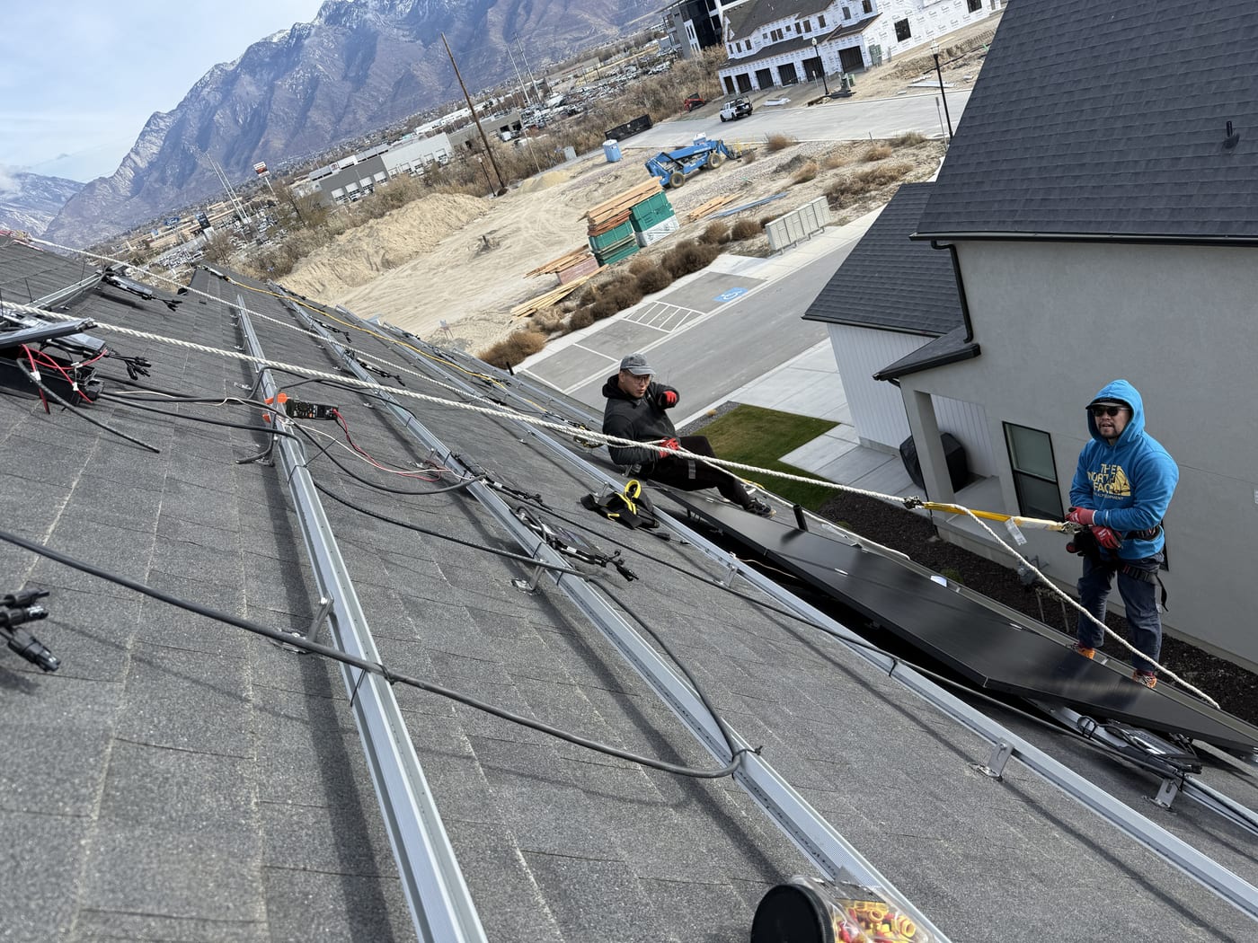 Close-up of crew member connecting microinverter wiring on racking rails, roof-level perspective