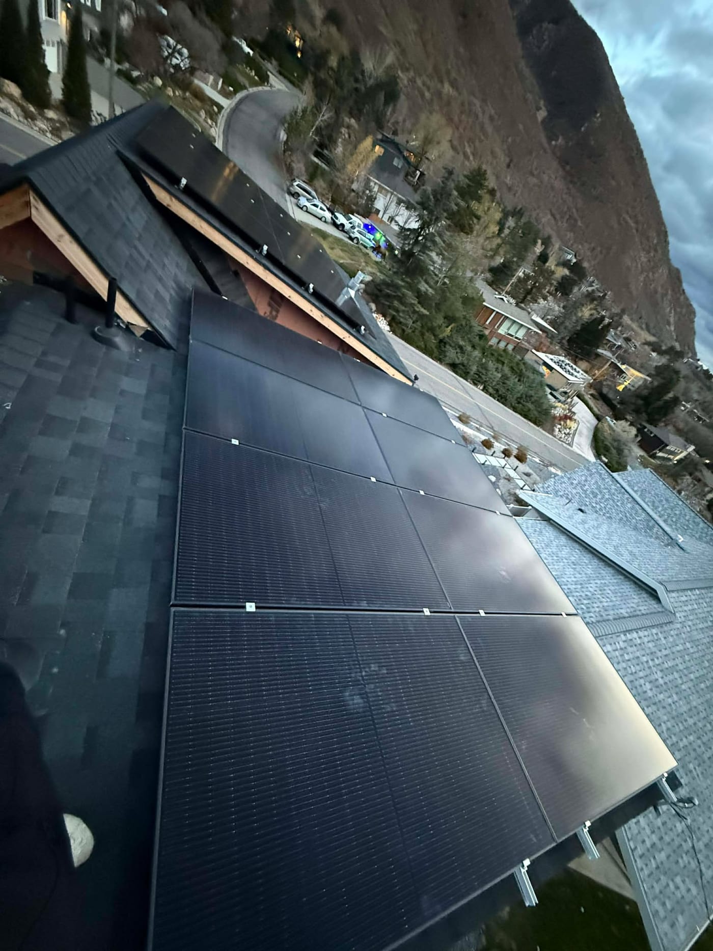Looking down at solar panel array on steep roof with neighborhood and mountain canyon visible below