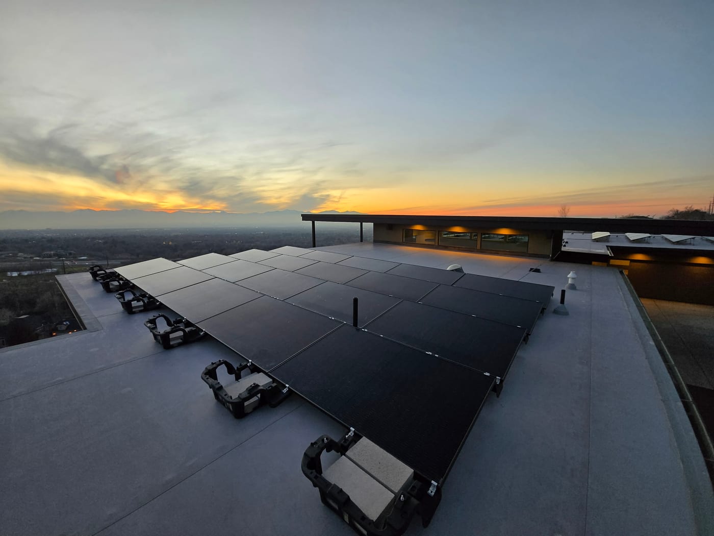 Wide view of ballasted solar array on flat roof at sunset, modern mid-century style home visible, valley panorama below
