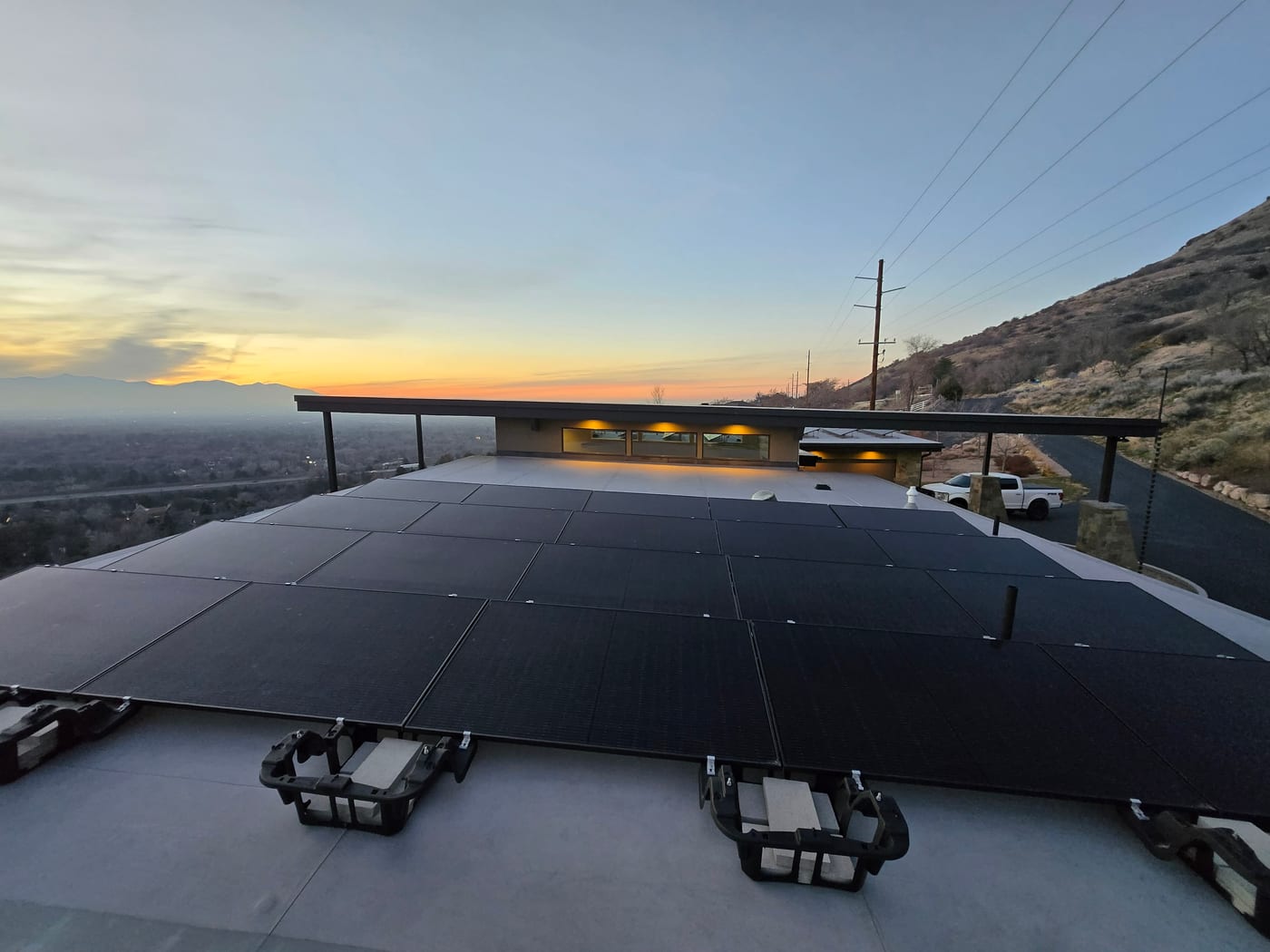 Ballasted flat-roof solar array with sunset sky, hillside and modern home architecture visible, truck in driveway