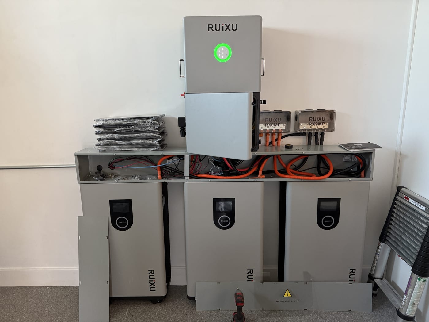RUiXU battery system with 3 stacked battery units, inverter, and RX9MP junction boxes mounted on interior wall, all units powered on with green LEDs