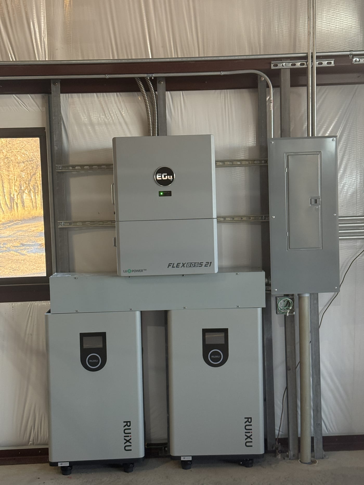 EG4 FlexBOSS 21 with two RUiXU batteries on unistrut rack, electrical panel above, vapor barrier wall