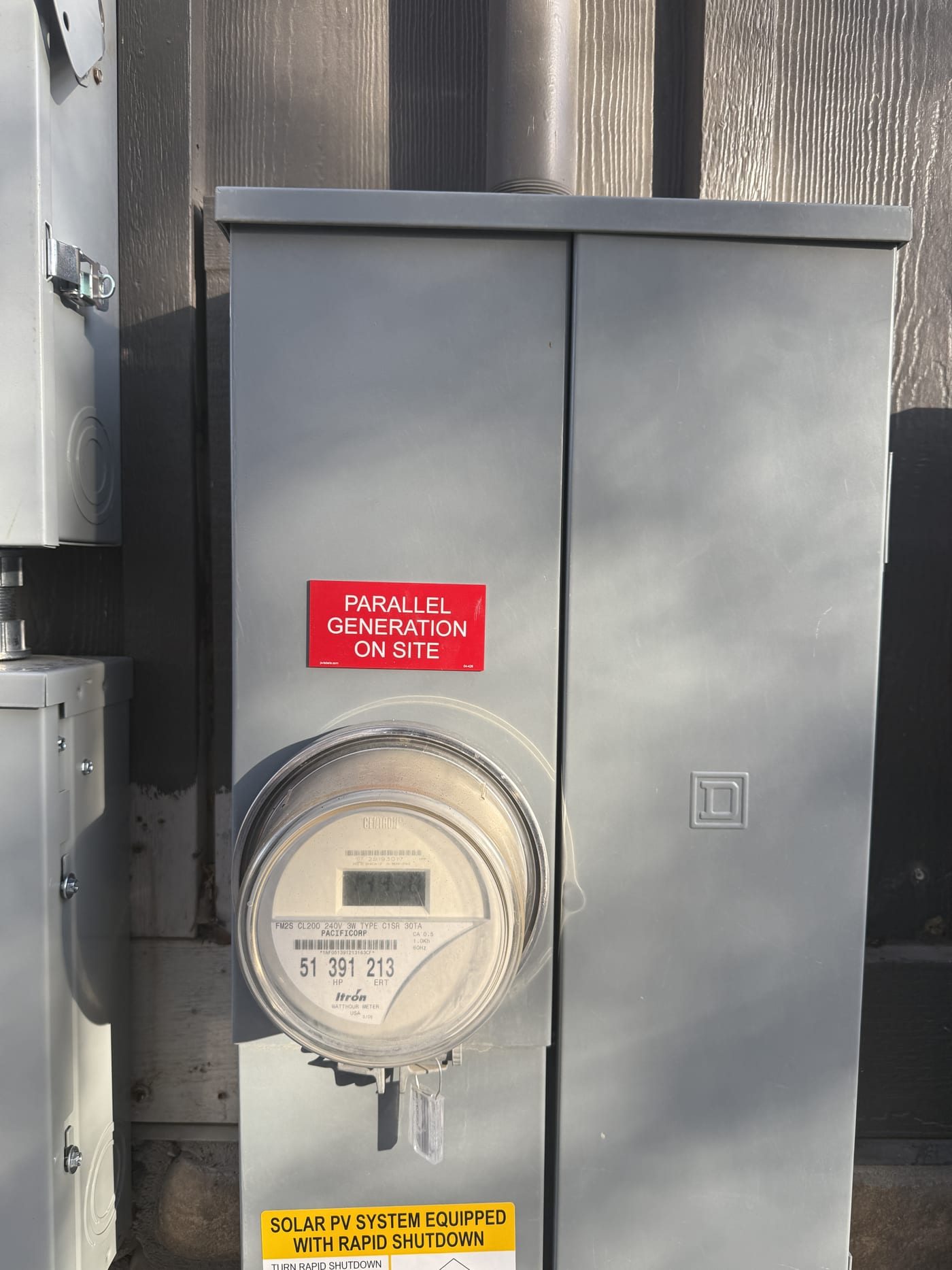 Close-up of utility meter with red Parallel Generation on Site sticker and yellow Solar PV System Equipped with Rapid Shutdown label