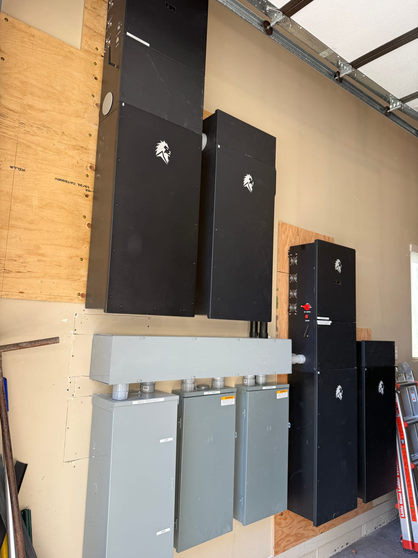 Different angle of staged Lion Energy Sanctuary battery system components on garage floor pre-installation, showing battery cabinets and disconnect panels